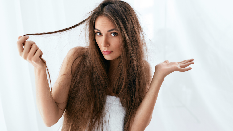 A woman examining her dry, damaged hair at home